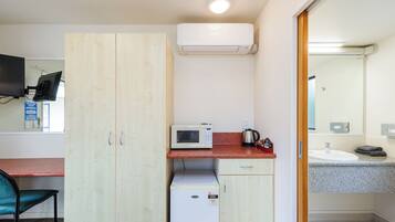 Una habitación compacta con kitchenette, microondas, refrigerador pequeño, armario de madera, escritorio con silla y baño con lavamanos y espejo.