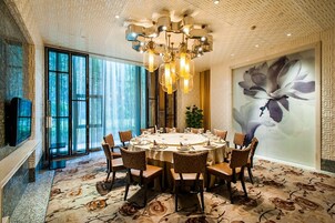 Un comedor con una mesa redonda dispuesta para ocho personas, rodeada de sillas, una araña y un cuadro grande con motivos florales en la pared.