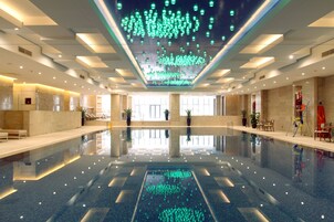 Una amplia piscina cubierta con suelo reflectante, rodeada de zonas de estar y plantas en macetas.
