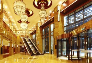 Un amplio vestíbulo con una escalera mecánica central, grandes candelabros y una entrada moderna de vidrio.