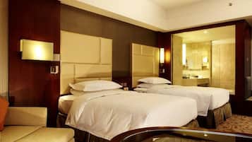 Two single beds with white linens and a wooden headboard, complemented by a seating area with a cushioned chair and glass coffee table.