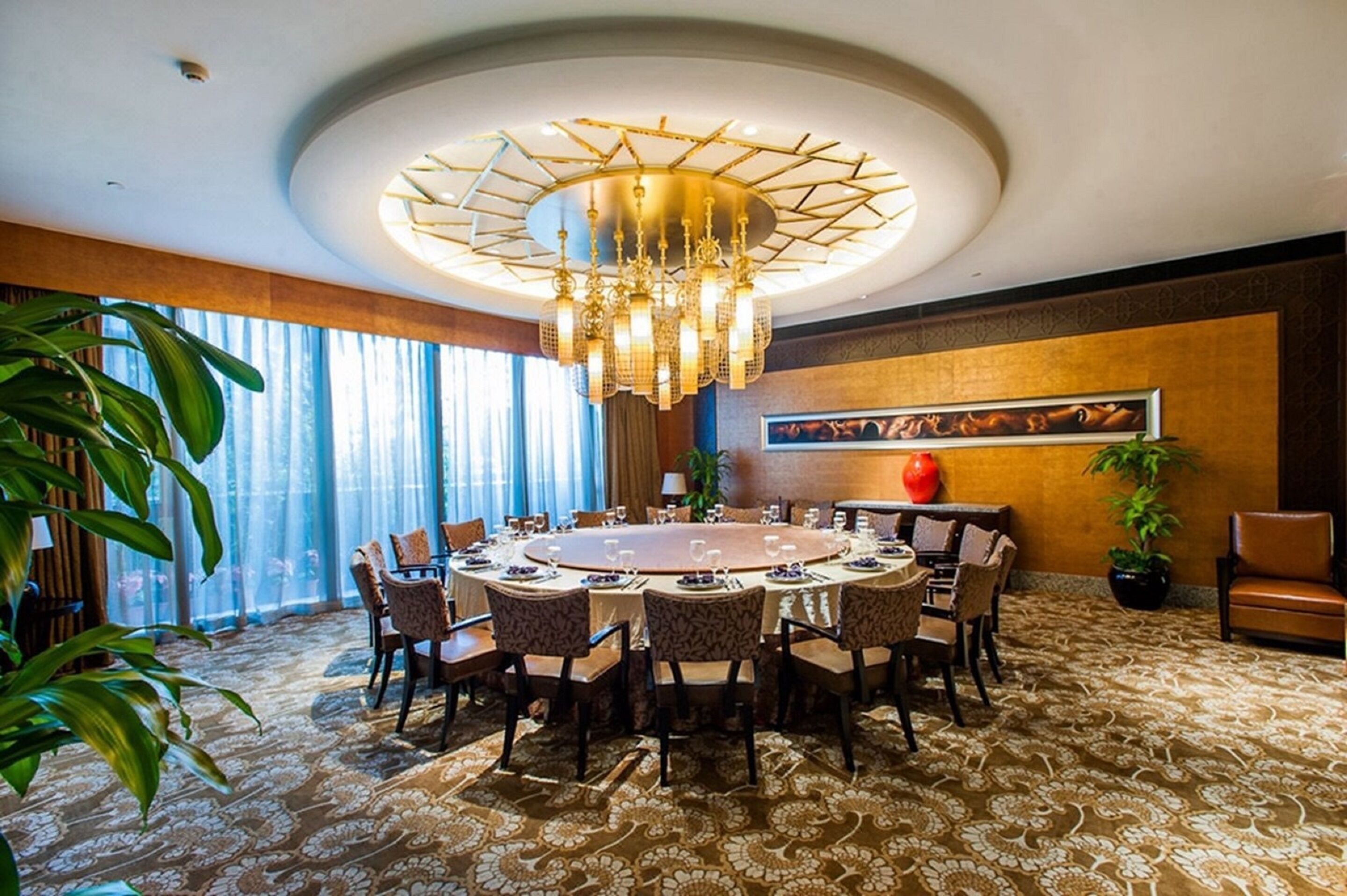 A round dining table set for eight with chairs, a chandelier, and a large window with curtains.