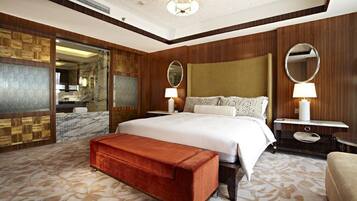 Habitación de hotel con una cama grande, dos mesitas de noche con lámparas, un cabecero de madera, un banco y un espejo amplio.