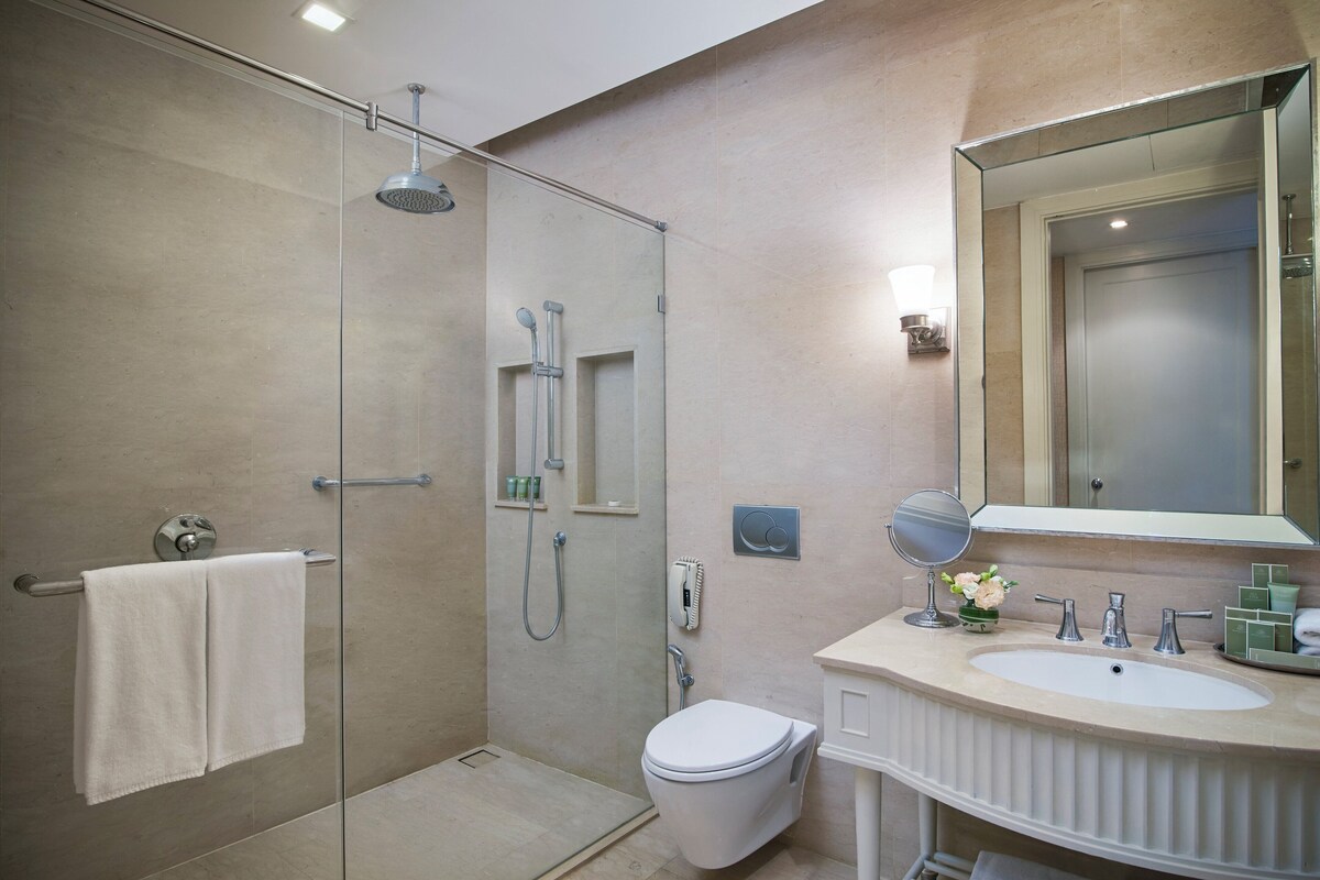 Un baño moderno con ducha de vidrio, inodoro y tocador con espejo y lavabo.