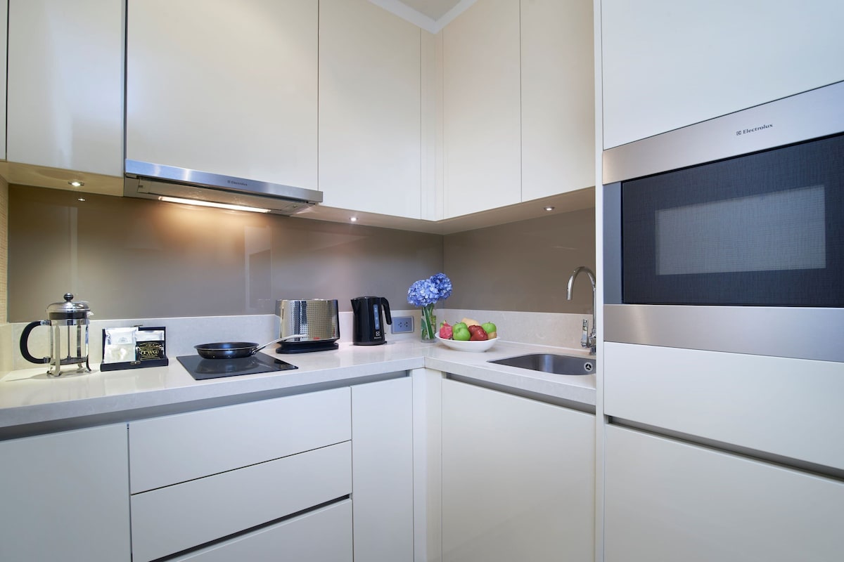 Una cocina moderna con armarios blancos, electrodomésticos de acero inoxidable, microondas y cafetera.