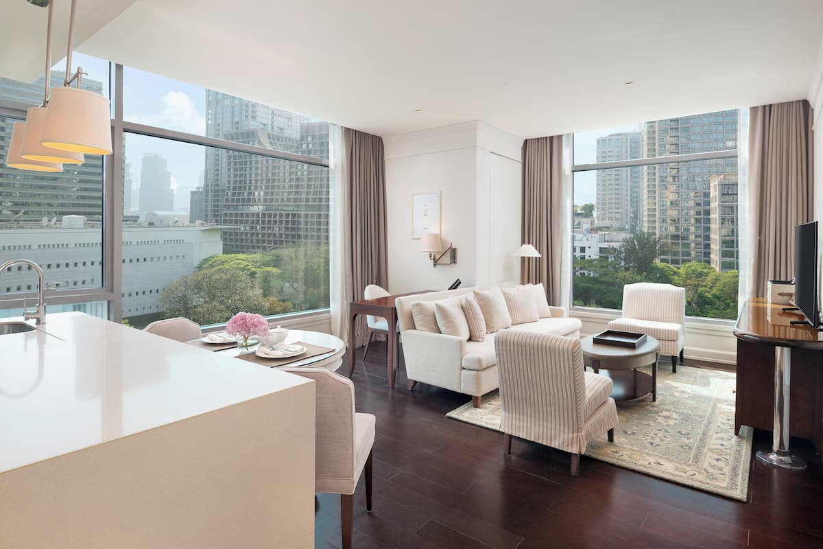 A modern hotel room with a large window, a sofa, a dining area, and a TV.