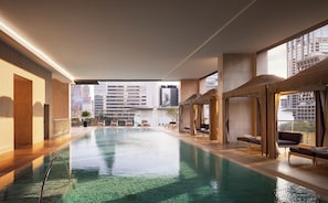 An indoor swimming pool with clear water, surrounded by lounge chairs and a view of tall buildings. - Oriental Residence Bangkok (Bangkok)