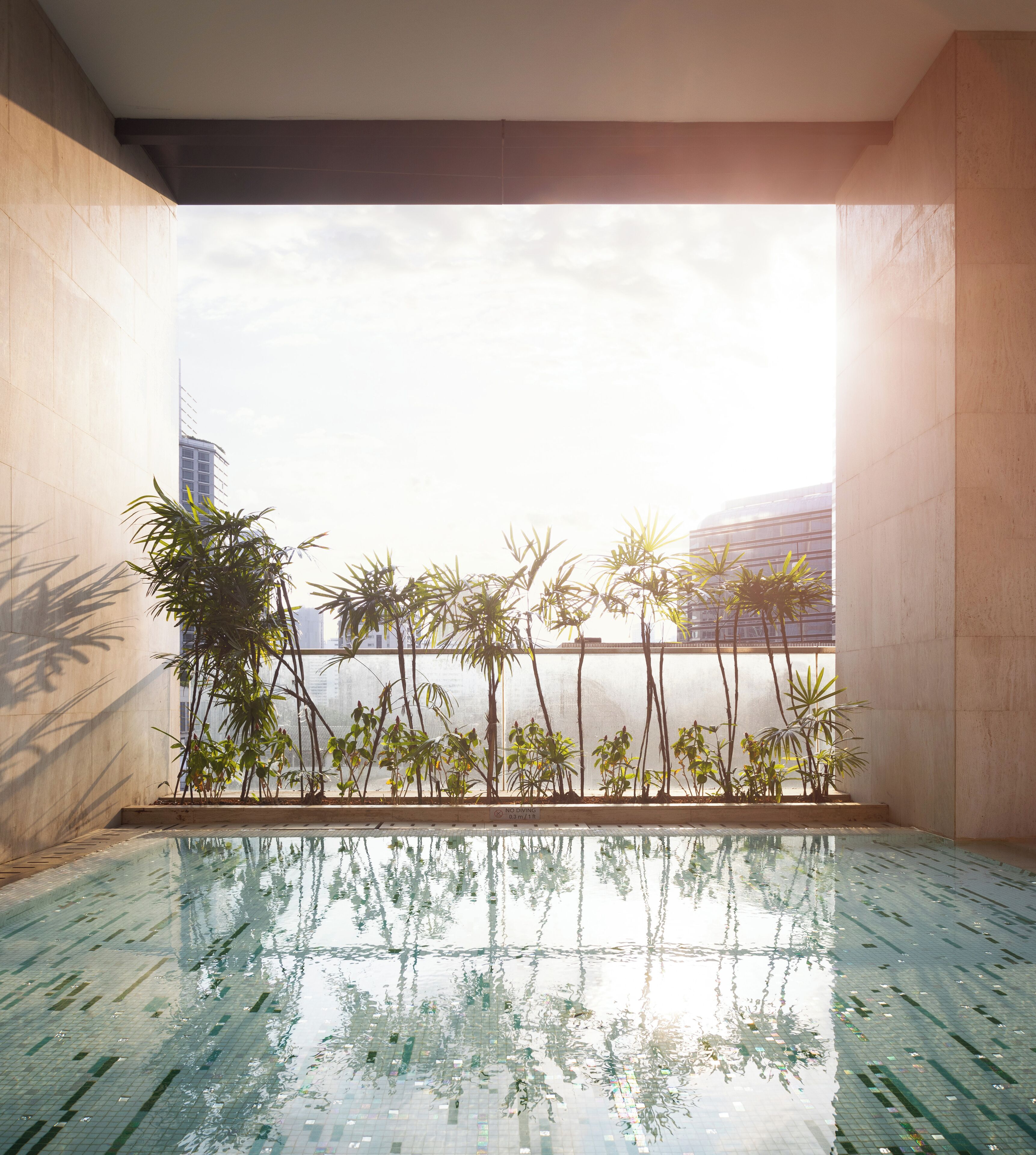 A pool area with tiled flooring and a view of tall buildings and palm trees.