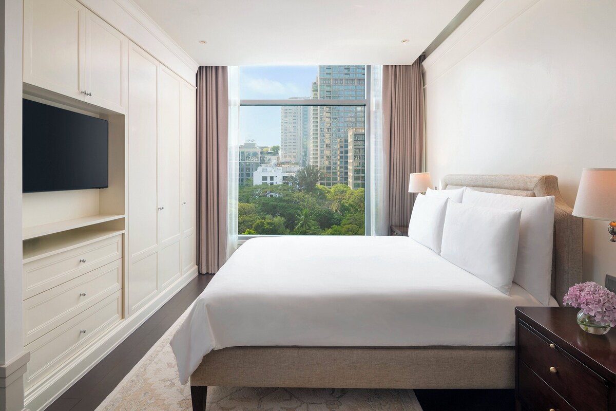 Habitación de hotel con una cama grande, un televisor montado en la pared y vistas de la ciudad a través de la ventana.