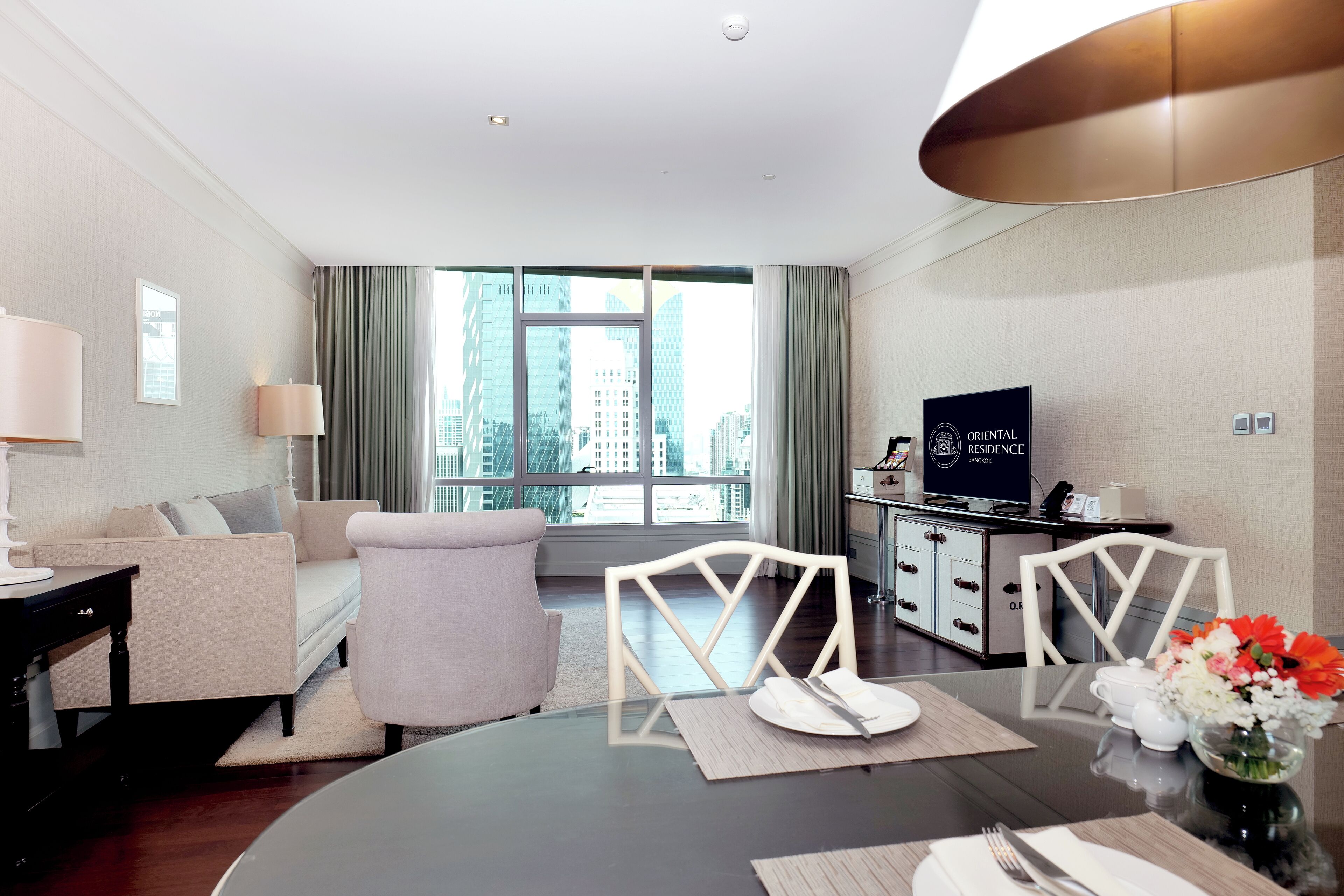 Une chambre d’hôtel moderne équipée d’un canapé, de fauteuils, d’une table à manger, d’un téléviseur et offrant une vue sur la ville.