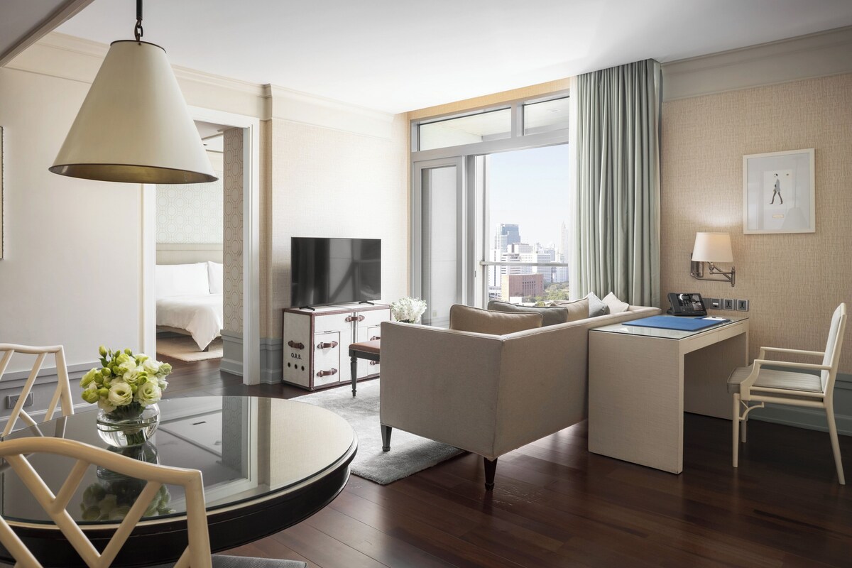 Une chambre d’hôtel moderne équipée d’un canapé, d’un bureau, d’une télévision et d’une grande fenêtre donnant sur la ville.