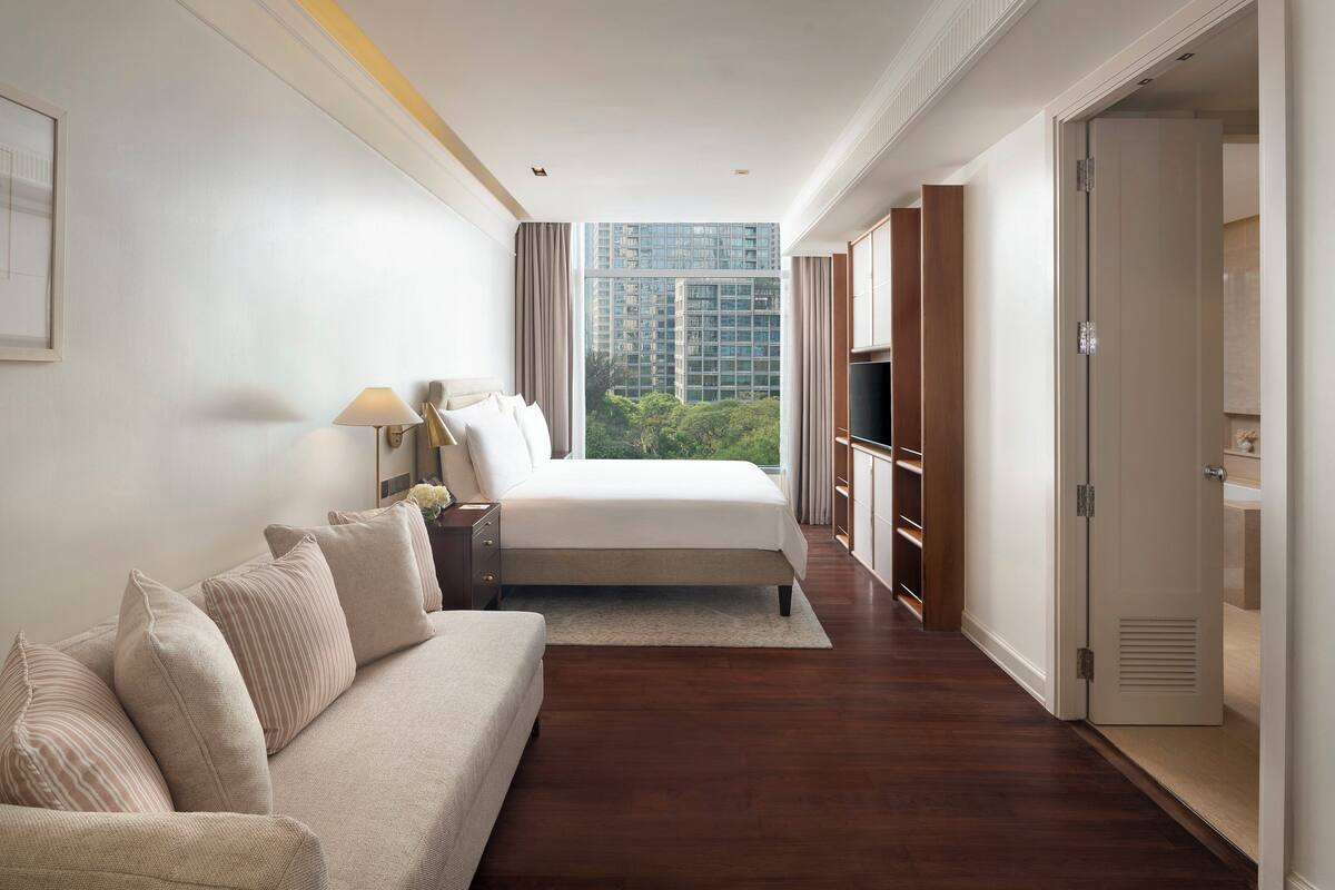 Habitación de hotel con cama, sofá, televisión y vistas a la ciudad.
