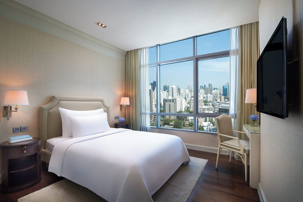 A hotel room with a large bed, a desk, a chair, a TV, and a view of a cityscape.