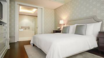 Hotelkamer met een groot bed, een nachtkastje met lamp, een kast en een badkamer door een open deur zichtbaar.