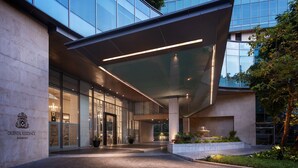 Un edificio moderno con fachada de vidrio, un acceso cubierto y un área ajardinada con plantas.