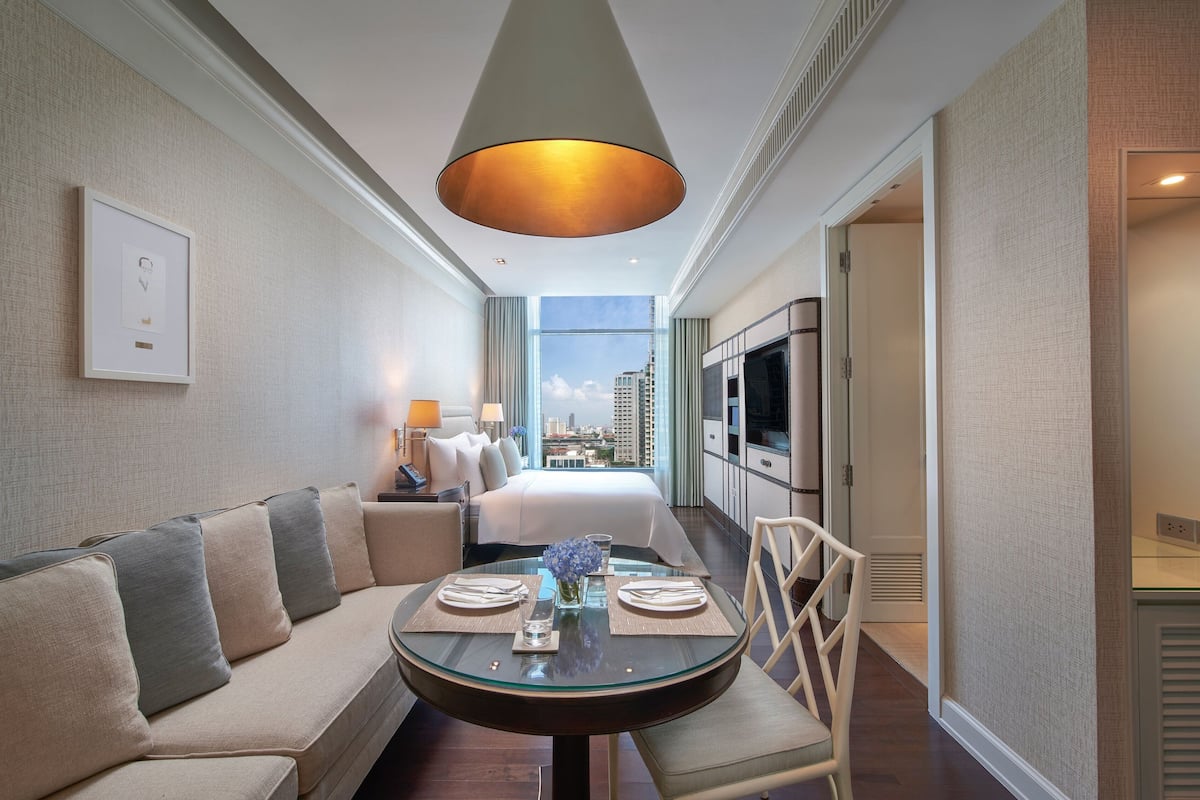 Una habitación de hotel con sofá, una mesa redonda de vidrio dispuesta para comer, cama con vistas y televisión.