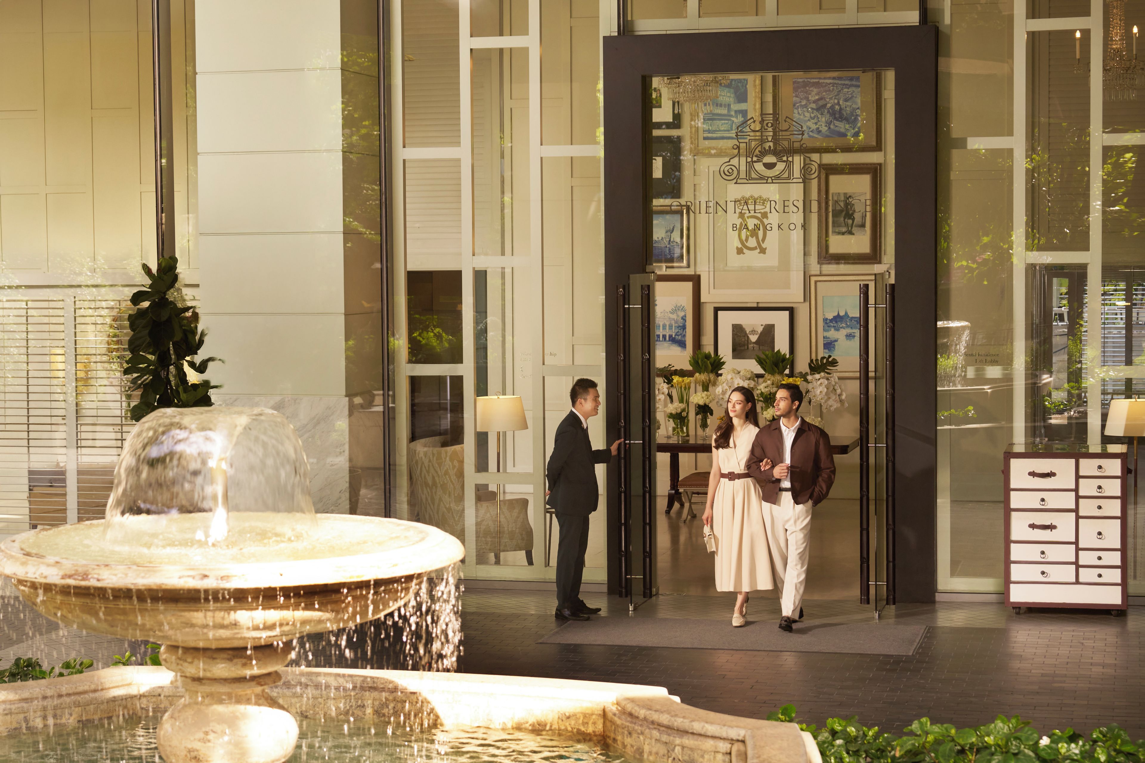 A hotel entrance with a fountain, a reception desk, and framed artwork on the walls.