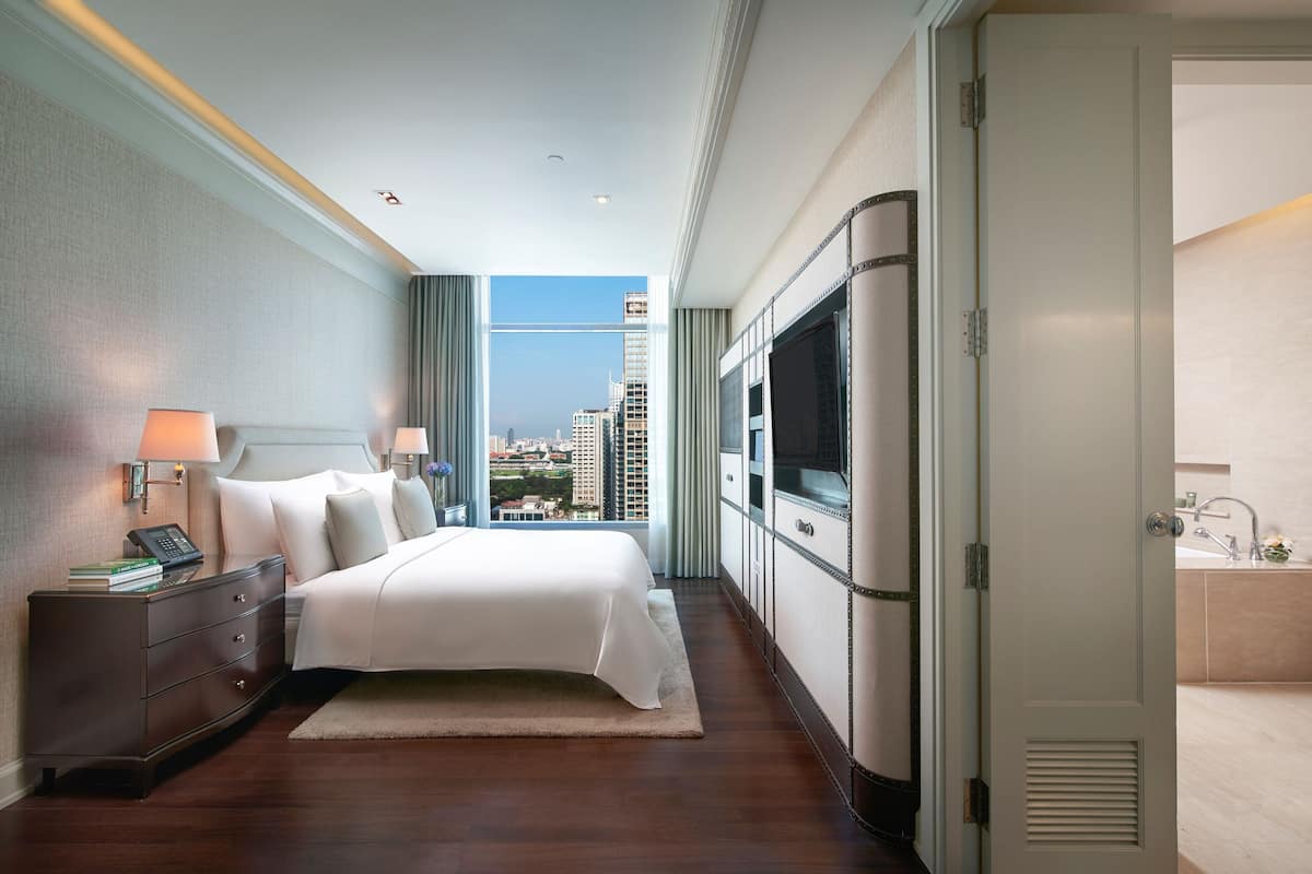 Habitación de hotel con una cama grande, televisión, escritorio con lámpara y vista a la ciudad.