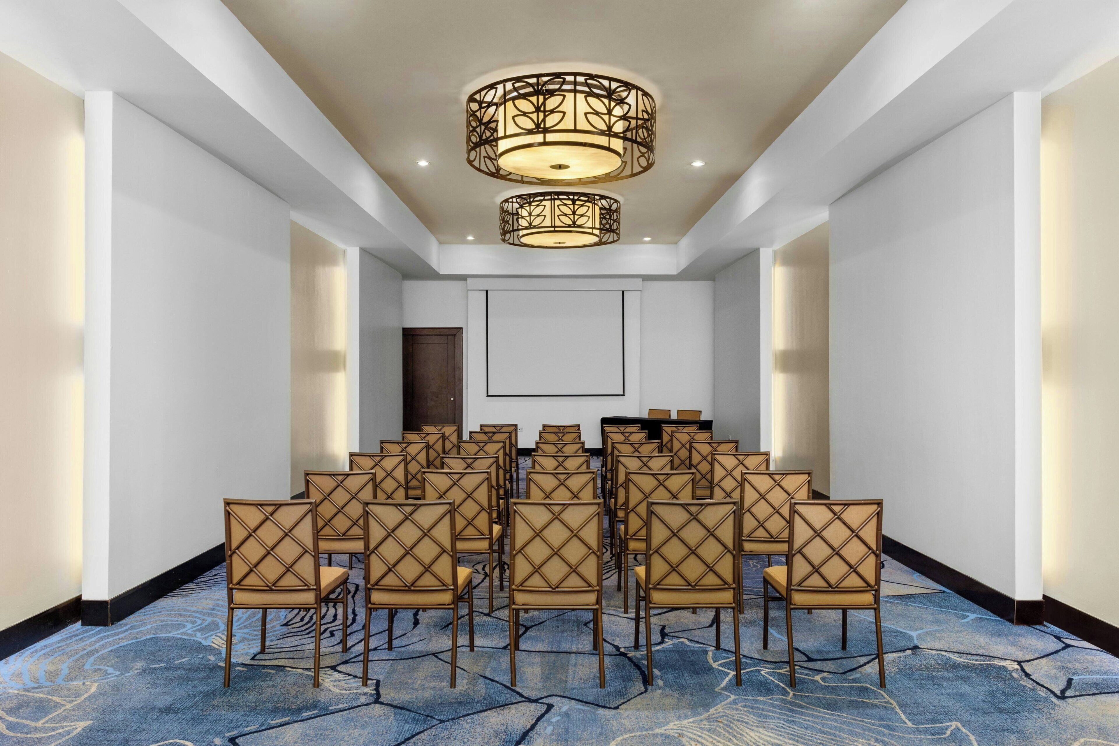 A conference room with rows of chairs, a large screen, and a decorative ceiling light fixture.