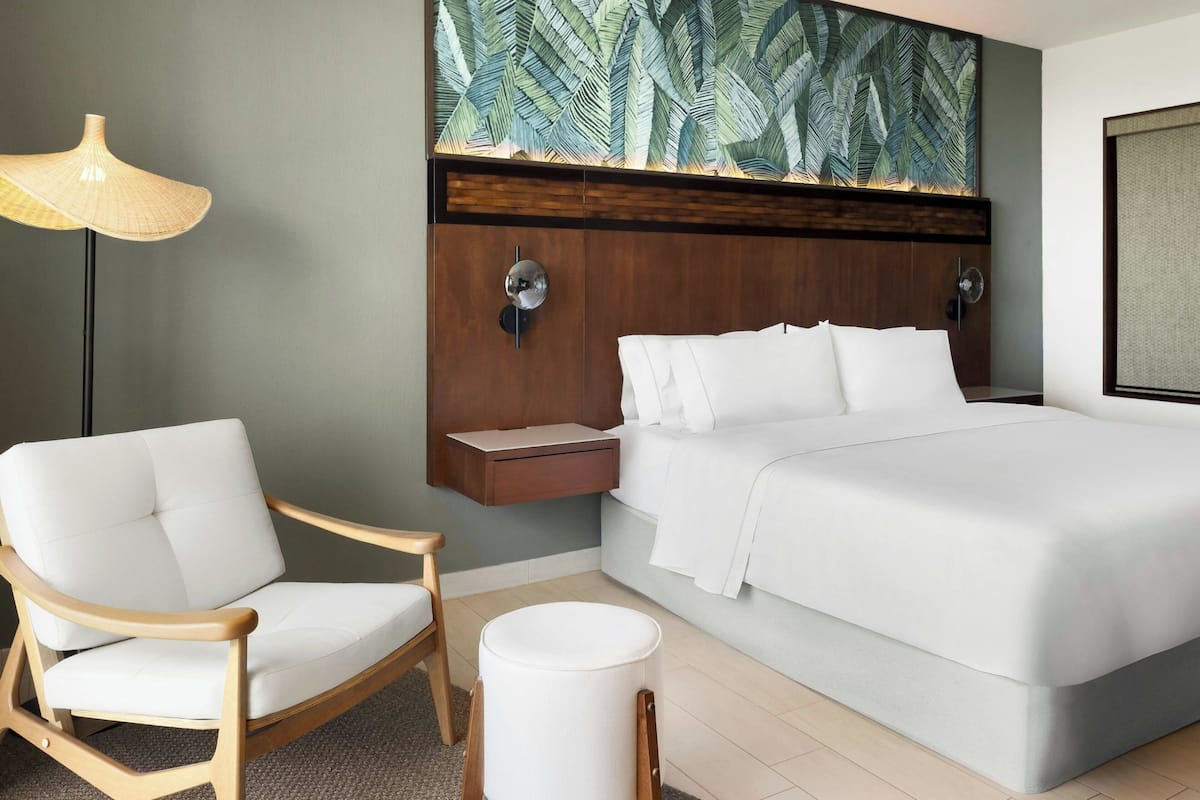 A modern hotel room with a bed, a wooden chair, a bedside table, and a large wall art piece.