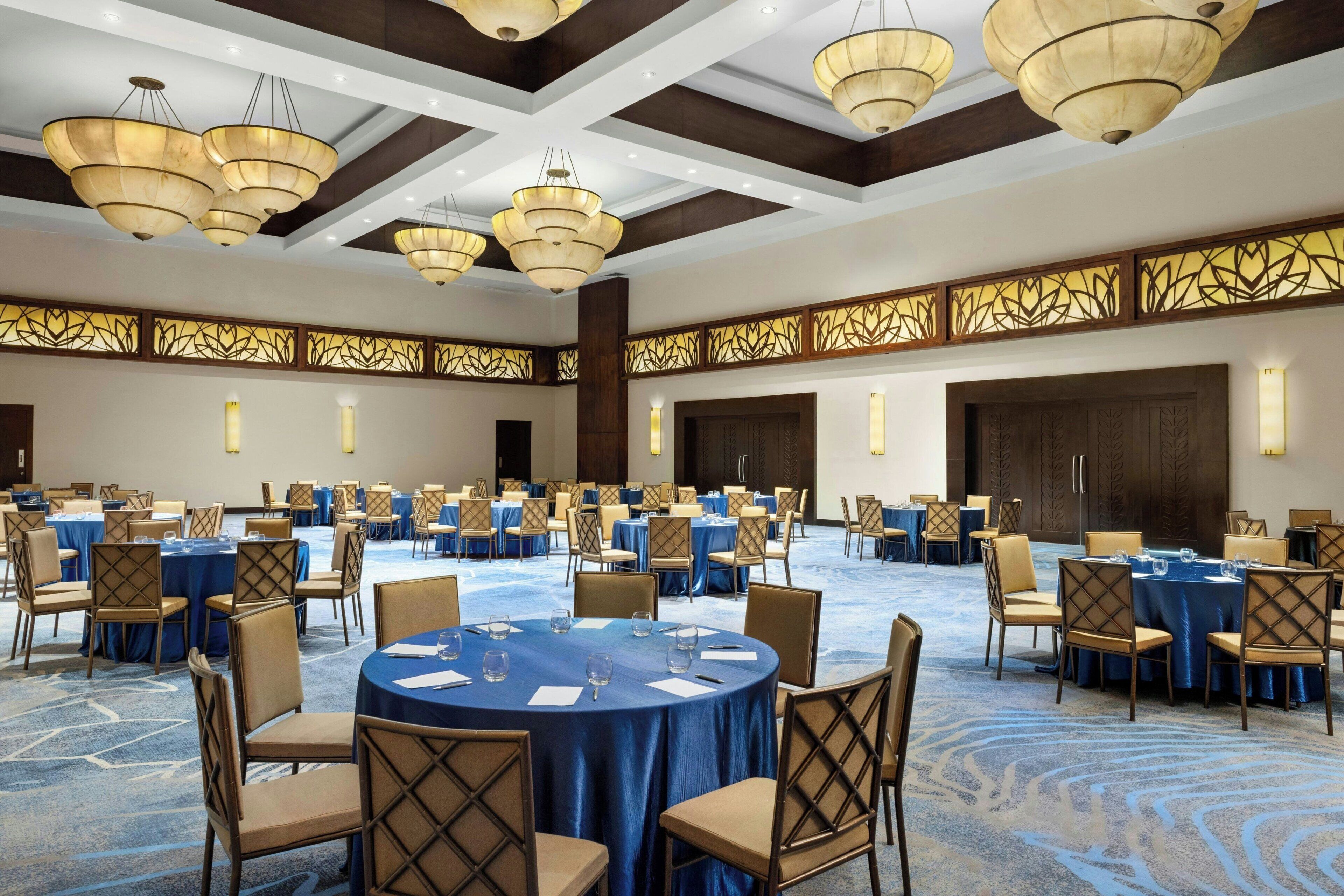 A large conference room with round tables, blue tablecloths, and beige chairs.