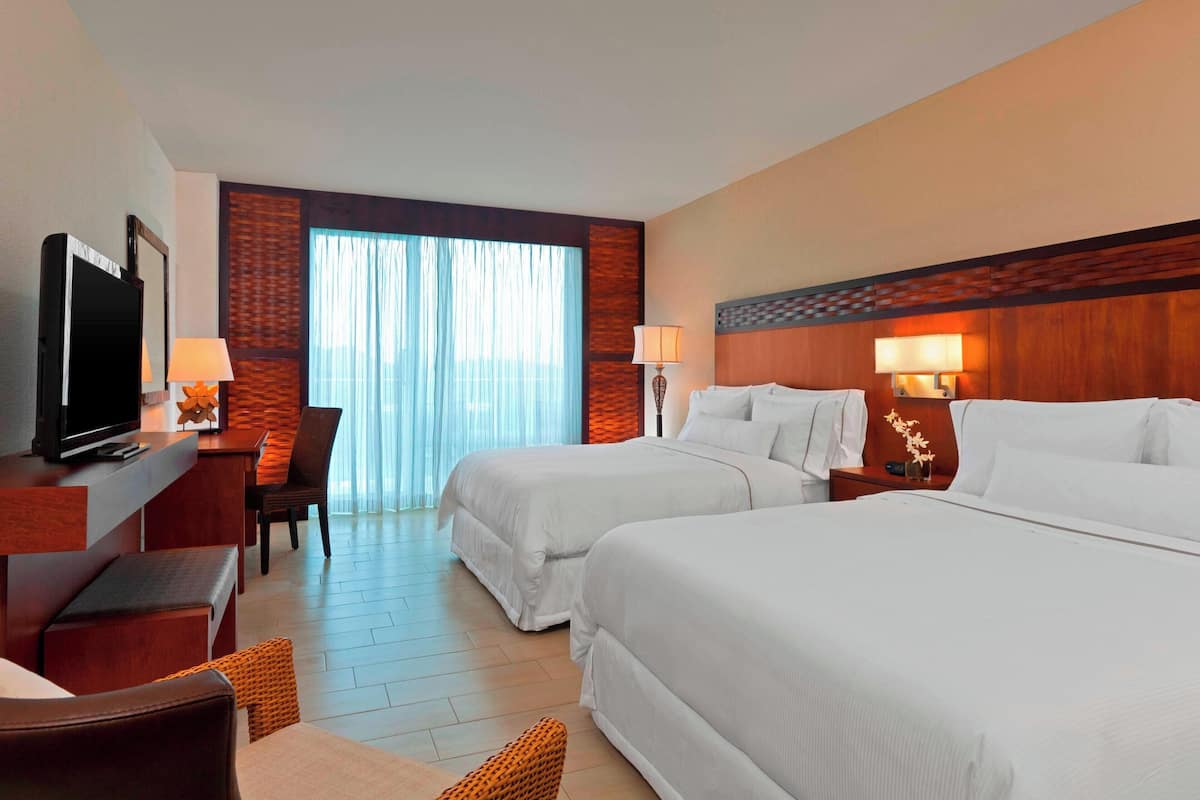 A hotel room with two beds, a desk with a TV, and a chair.