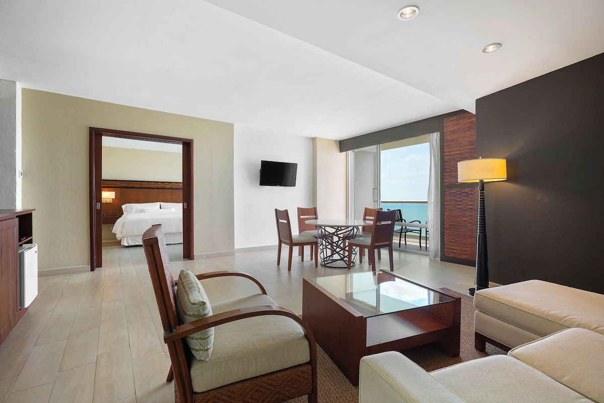 A hotel room with a bed, a TV, a dining area with chairs and a table, and a sofa.