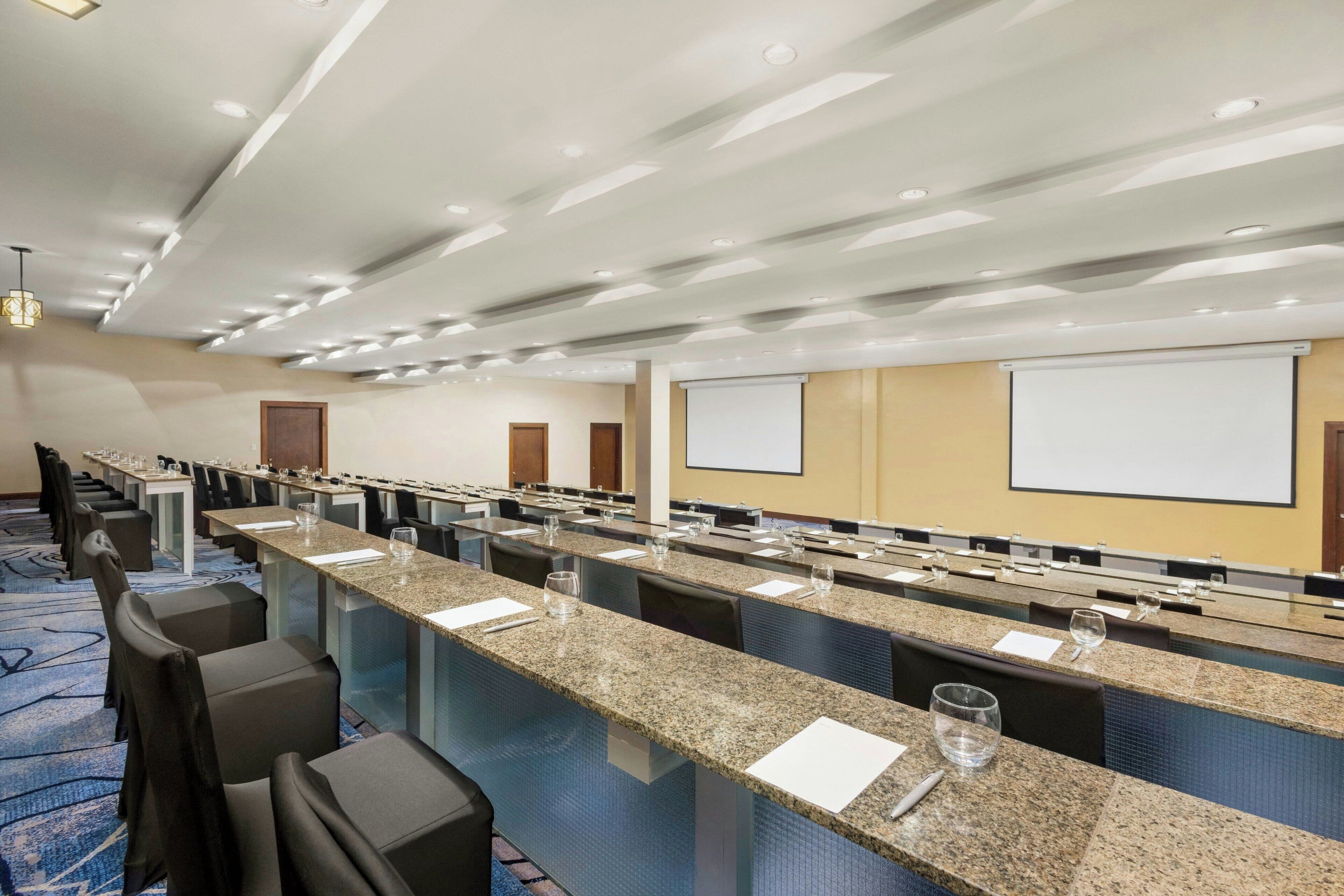 A conference room with long tables, chairs, and a projector screen.
