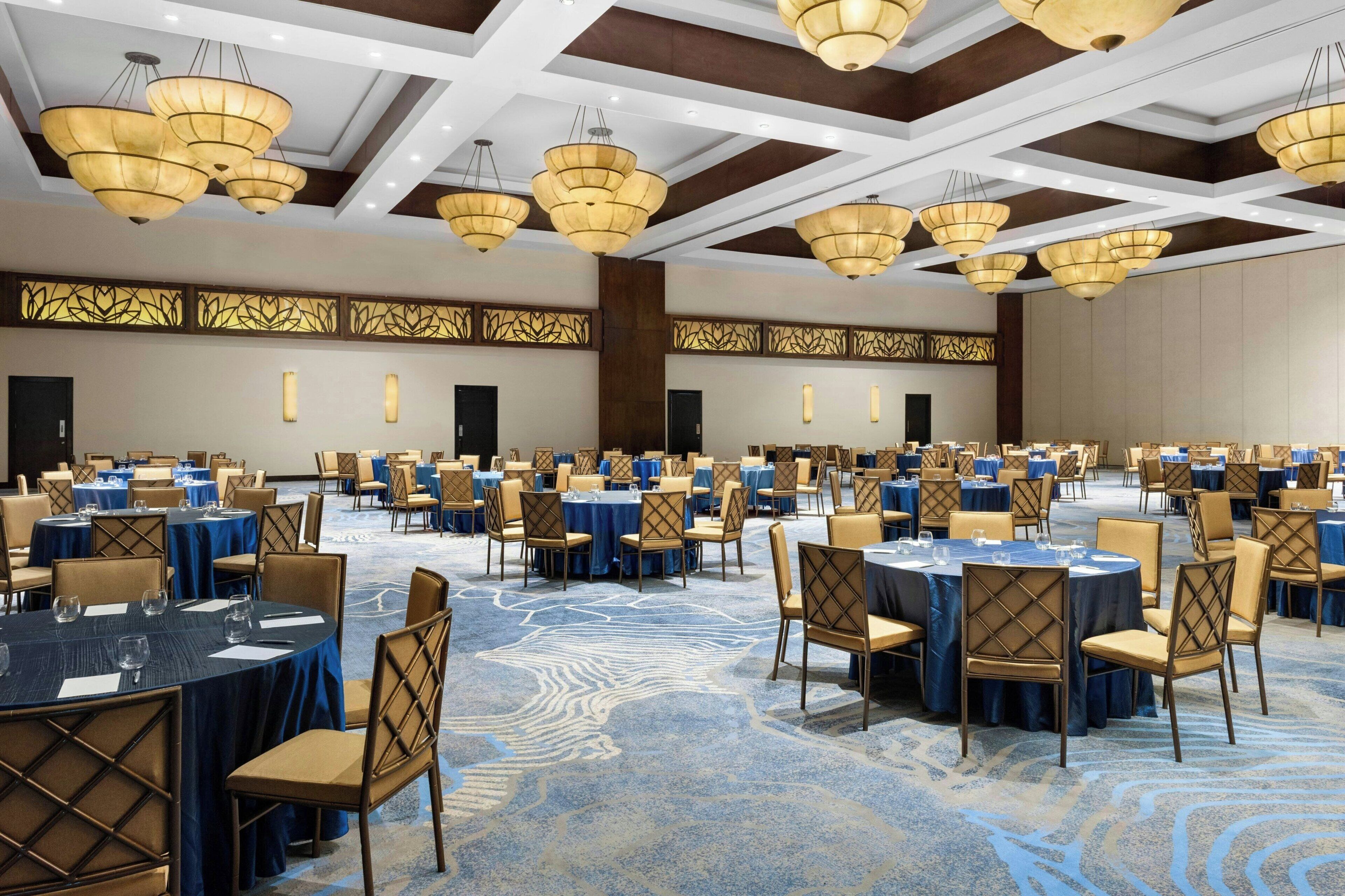 A large banquet hall with round tables, chairs, and chandeliers.