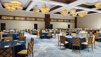 A large banquet hall with round tables, chairs, and chandeliers.