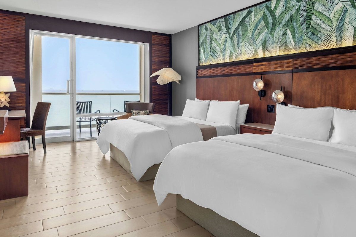 A hotel room with two beds, a balcony with a view, and a large window.