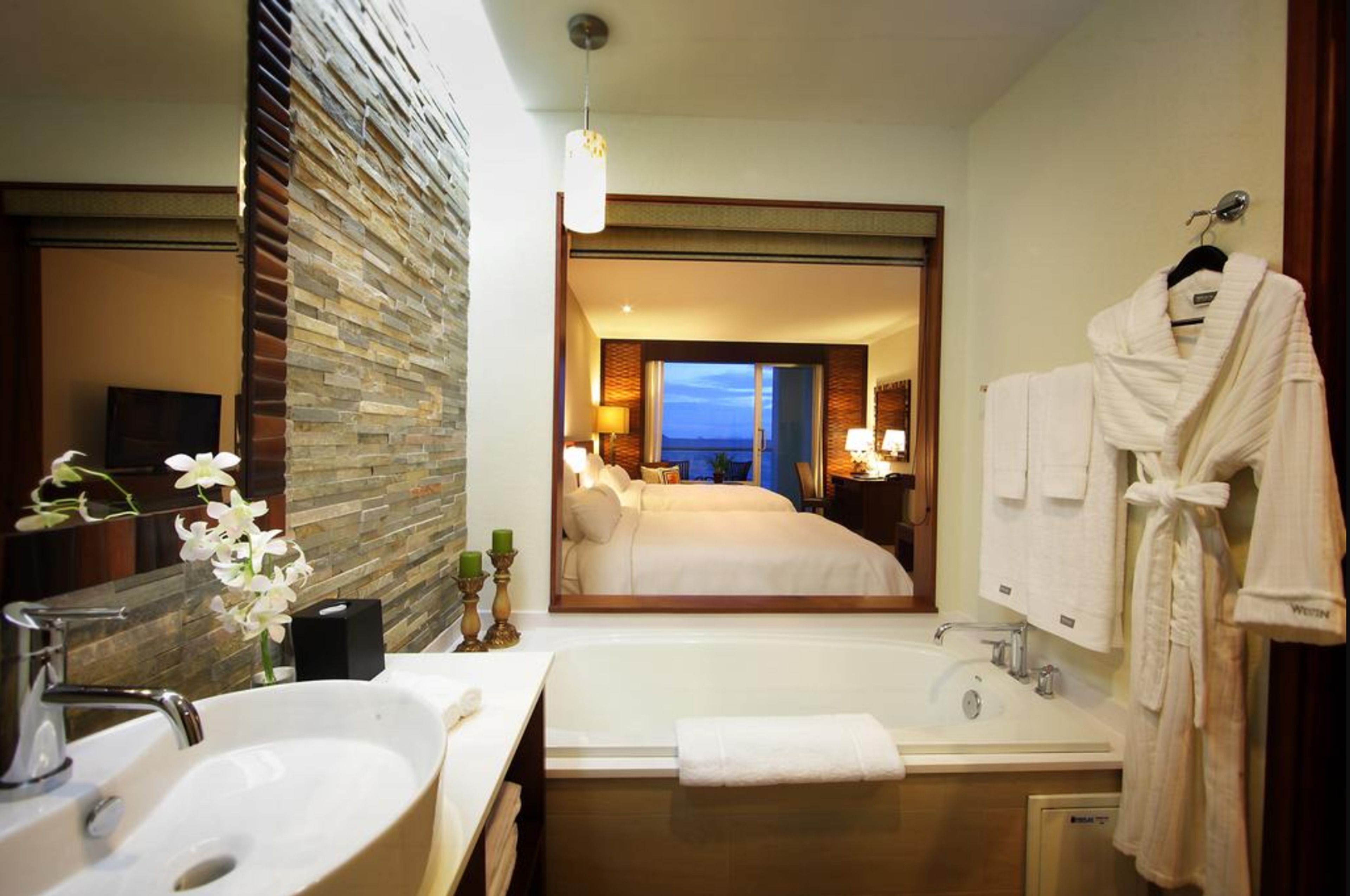 A hotel bathroom with a large mirror, a bathtub, and a sink.