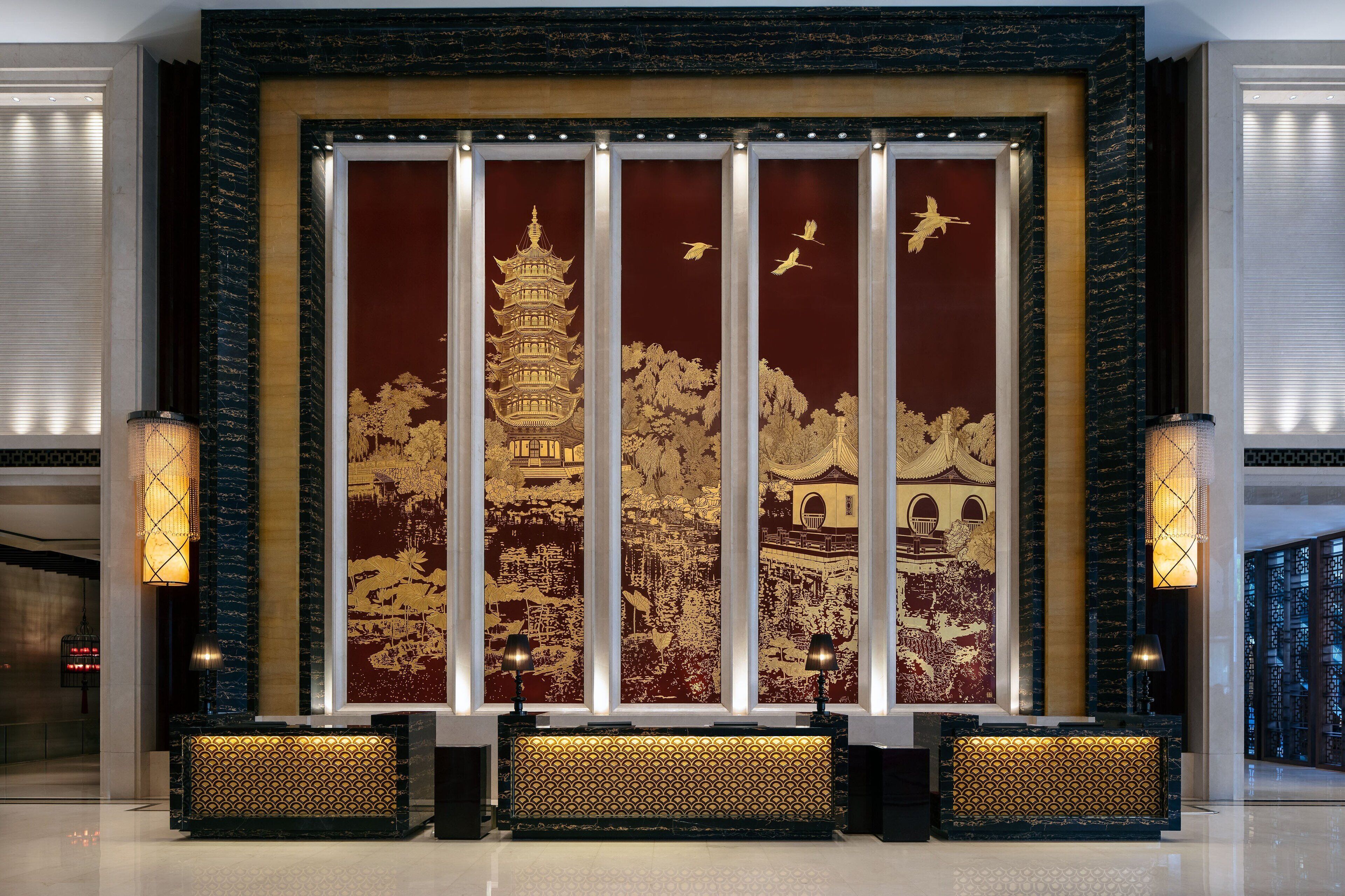 Un área de recepción con un gran mural de una pagoda y pájaros, dos lámparas de pie y un mostrador de recepción.