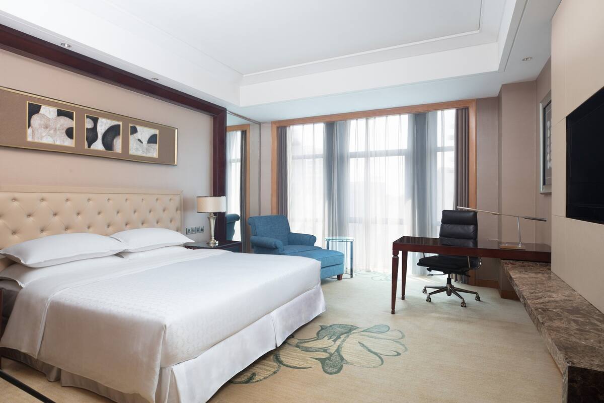 Une chambre d’hôtel avec un grand lit, un bureau, une chaise et un téléviseur.