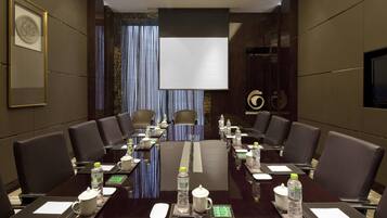 Una sala de conferencias con una mesa larga, sillas, botellas de agua y una pantalla de proyector.