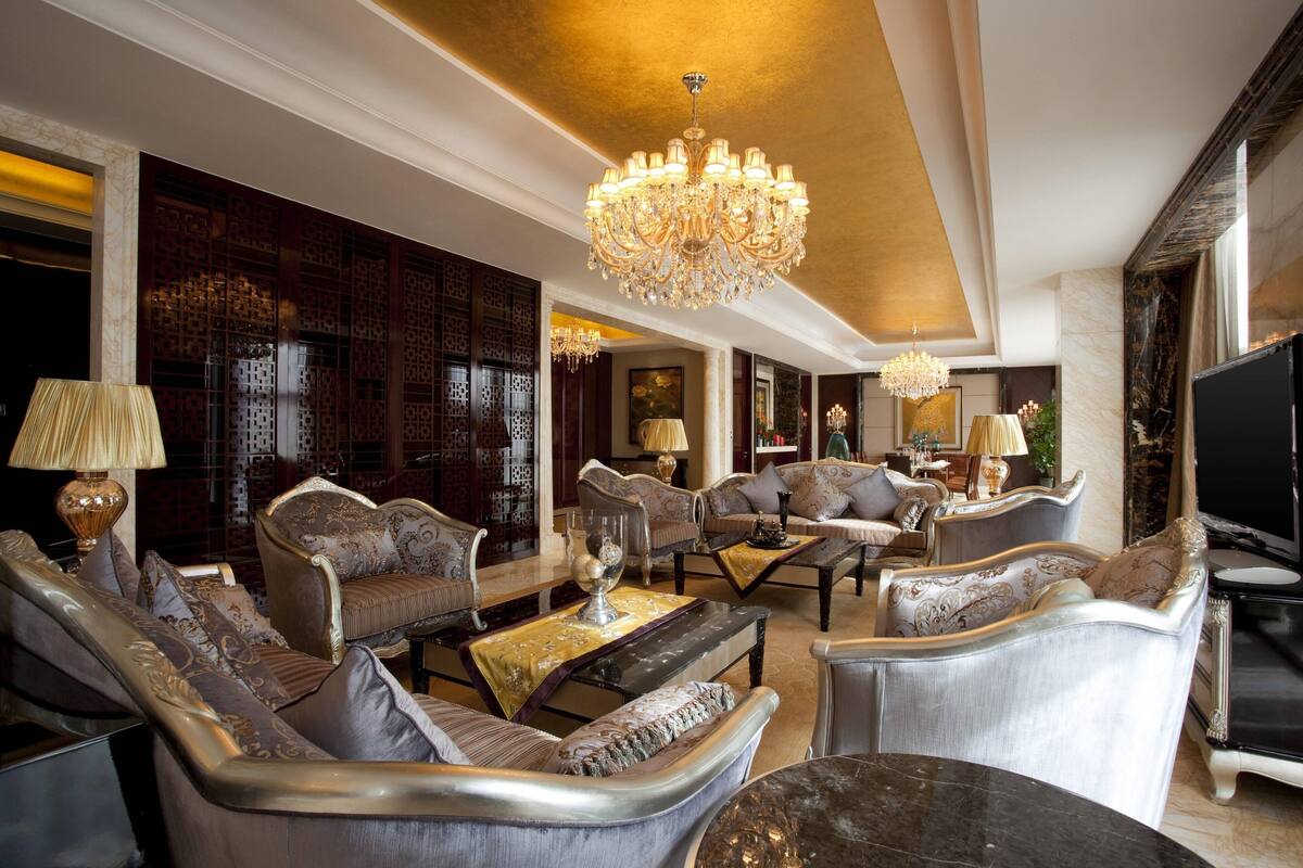 Un salon luxueux, agrémenté de meubles élégants, d’un grand lustre et d’un téléviseur.