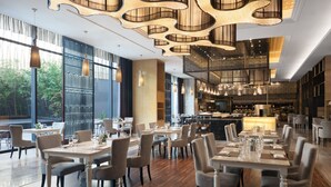 Ein großzügiges Restaurant mit hohen Decken, modernen Kronleuchtern und großen Fenstern mit Blick ins Freie.