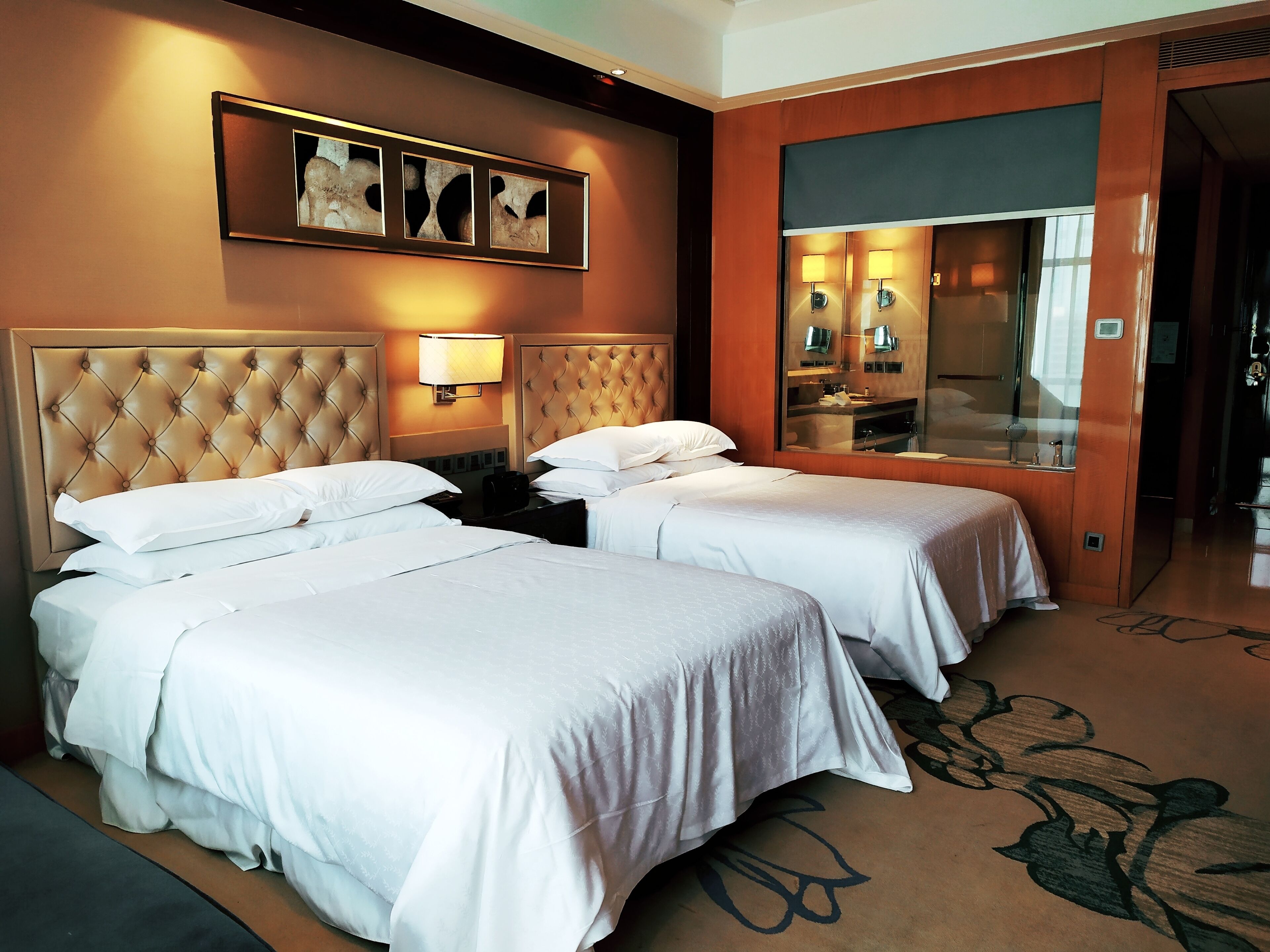 A hotel room with two beds, a large mirror, and a wall-mounted artwork.