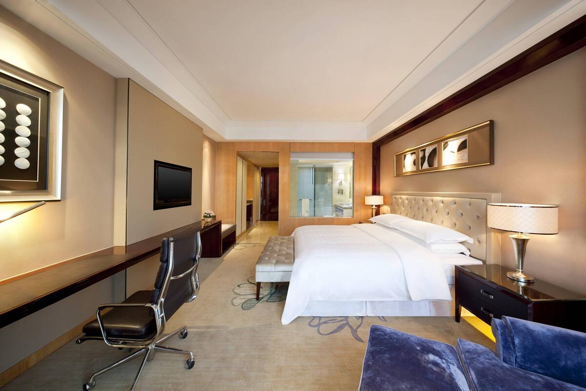 Une chambre d’hôtel avec un grand lit, un bureau avec une chaise, une télévision et une salle de bain visible au fond.