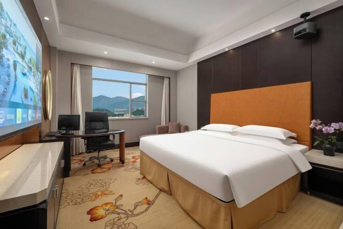 A hotel room with a bed, desk, chair, and a large window with a view.
