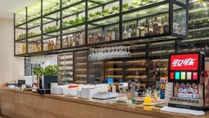 Zona de bar con estantes llenos de botellas, una máquina de café y un dispensador de bebidas.