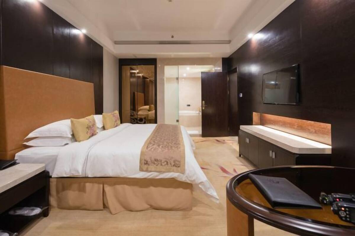 A modern hotel room with a large bed, a bedside table, a TV mounted on the wall, and a small seating area with a table and chairs.