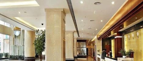 A hotel lobby with a reception desk, a large column, and a plant.