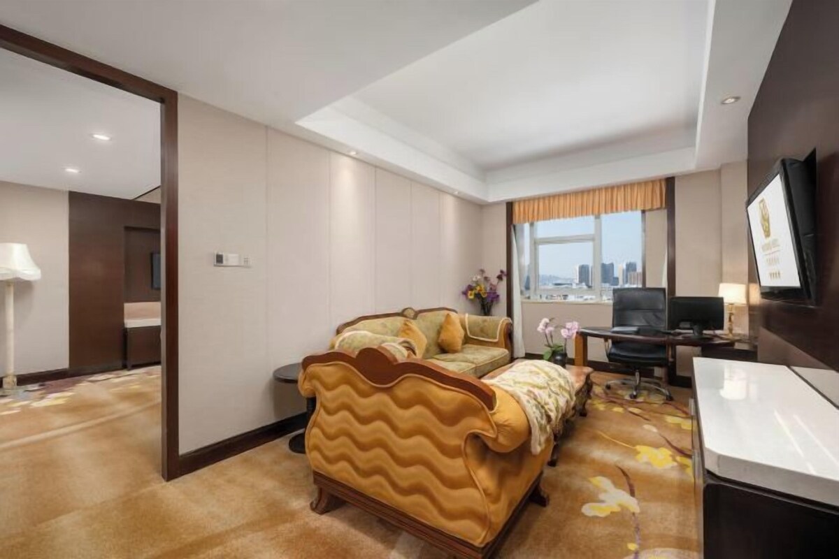 A hotel room with a large bed, a desk, a chair, a TV, and a window with a city view.
