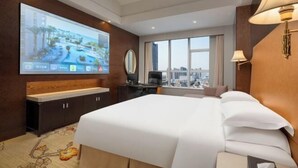 Habitación de hotel con una cama grande, un televisor montado en la pared, un escritorio con una silla y una ventana con vistas a la ciudad.