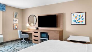 A hotel room with a bed, a desk with a computer, a flat-screen TV, a mirror, and artwork on the walls.