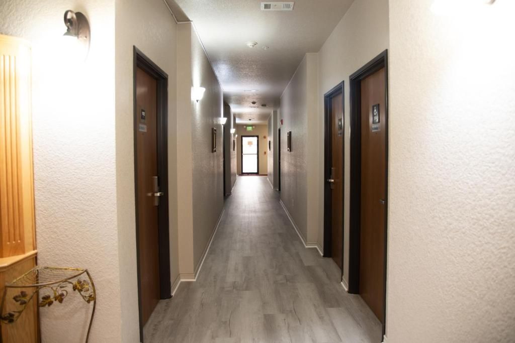 A hotel hallway with wooden flooring, doors on both sides, and light fixtures along the ceiling.