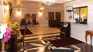 A hotel lobby with a chandelier, a reception desk, a TV, and a seating area with two chairs and a sofa. - Premium Inn and Suites (Killeen)