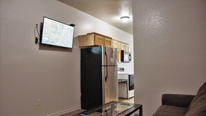 A compact living space with a kitchenette, a flat-screen TV mounted on the wall, and a glass-top coffee table. - Premium Inn and Suites (Killeen)