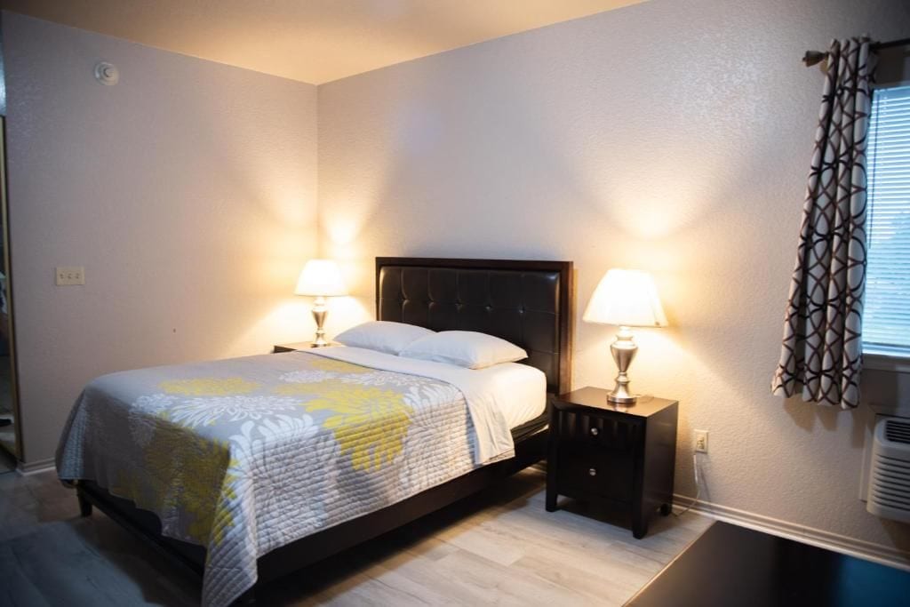 Een slaapkamer met een bed, nachtlampjes, een nachtkastje en een raam met gordijnen.